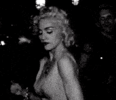 a black and white photo of a woman in a very revealing dress standing in a dark room .