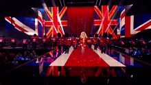 a woman in a red dress is walking down a red white and blue carpet surrounded by british soldiers