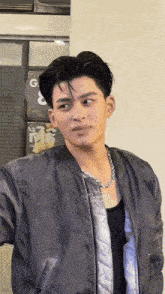 a young man wearing a bomber jacket and a necklace is standing in front of a sign that says g