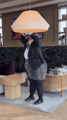 a woman in a leopard print skirt is holding a large lamp over her head