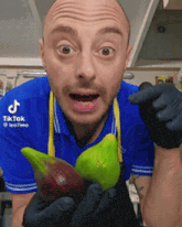 a man wearing a blue shirt and black gloves is holding a green and a red fruit ..