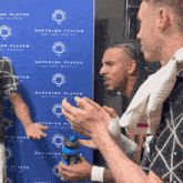 men clapping in front of a blue sign that says superior player of the match on it