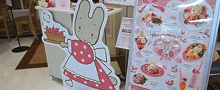 a cardboard cutout of a bunny holding a basket of strawberries stands in front of a menu for a cafe