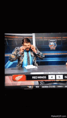 a man is sitting at a table with a red wings logo on it