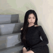 a woman in a black dress is sitting on a set of stairs and looking at the camera .