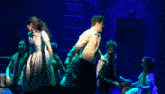 a group of people are dancing on a stage with blue lights