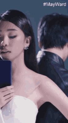 a woman in a white dress is looking at a phone with #mayward written on the bottom right