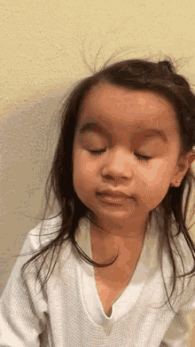 a little girl is making a funny face with her eyes closed and her hair blowing in the wind .