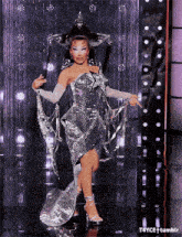 a woman in a silver dress and hat is dancing on a stage .