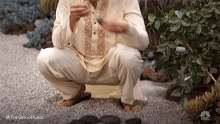 a man in a traditional dress is squatting down while eating a sandwich .
