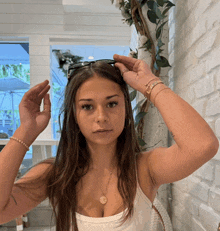 a woman adjusts her sunglasses while wearing a necklace that has a coin on it