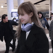 a woman wearing headphones and a black jacket is standing in a crowd .