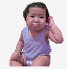 a baby in a blue tank top is sitting on a white surface .