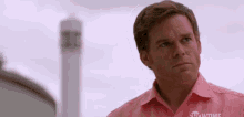 a man in a pink shirt is standing in front of a tower and looking at the camera .