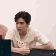 a young man is sitting at a table wearing a t-shirt that says taiyaki .