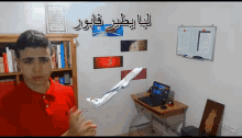 a man in a red shirt stands in front of a model airplane and a laptop