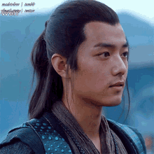 a young man with a ponytail and a scarf around his neck is looking at something