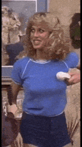 a woman in a blue shirt and blue shorts is standing in a room holding a remote control .