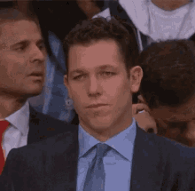 a man in a suit and tie is sitting in a crowd of people looking at something .