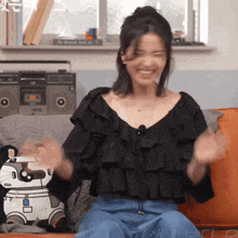 a woman in a black ruffled top is sitting on a couch in front of a boombox