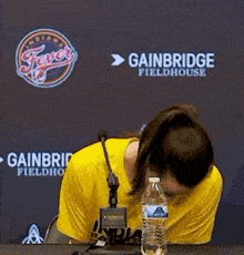 a woman in a yellow shirt is sitting at a table with a bottle of water .