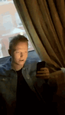 a man is sitting in front of a window looking at his cell phone