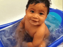a baby is taking a bath in a blue tub and smiling at the camera .