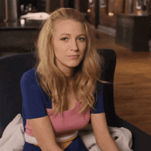 a woman in a blue and pink top sits in a chair and looks at the camera