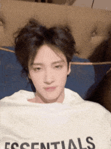 a young man is laying on a couch wearing a white essentials t-shirt .