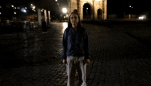 a woman is walking down a dark cobblestone street at night