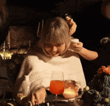 a woman sits at a table with a glass of orange liquid
