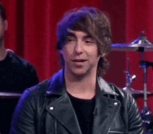 a man wearing a leather jacket is sitting in front of a drum set