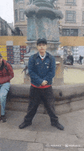 a man stands in front of a fountain wearing a hat with the letter n on it