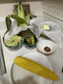 a corn on the cob sits on a white plate next to bowls of vegetables