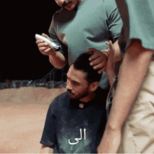 a man is getting his hair cut by another man who is wearing a shirt that says ali