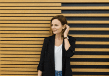 a woman in a black jacket stands in front of a wood paneled wall