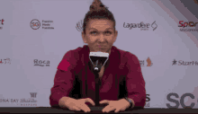 a woman sitting at a table with a microphone in front of a wall with logos for lagardere and roca