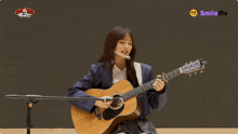 a woman playing an acoustic guitar in front of a microphone and smiling