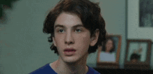 a close up of a young man 's face in a living room with pictures in the background .