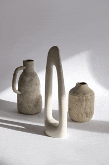 a vase with a handle sits next to two other vases on a white surface