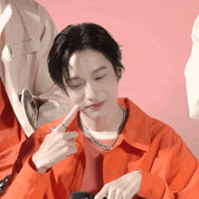 a man wearing an orange jacket and a silver necklace is making a face