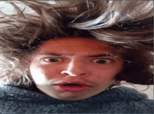 a man with his hair blowing in the wind is making a funny face .