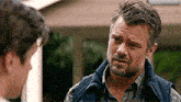 a man with a beard wearing a vest is talking to another man .