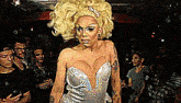 a drag queen in a white dress stands in a crowd of people