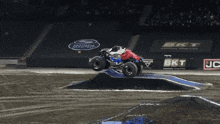 a monster truck is jumping over a dirt track in front of a bkt advertisement