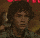 a young man with curly hair is looking at the camera in front of a red sign that says ' u ' on it