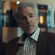a man with gray hair and a beard wearing a striped shirt and a brown jacket