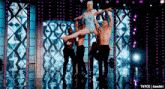 a woman is being lifted in the air by two men on a stage with purple lights behind them