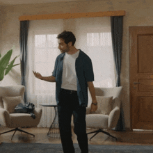 a man in a blue shirt and black pants stands in a living room