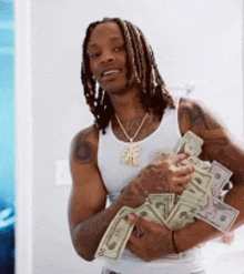 a man in a white tank top is holding a bunch of money in his hands .